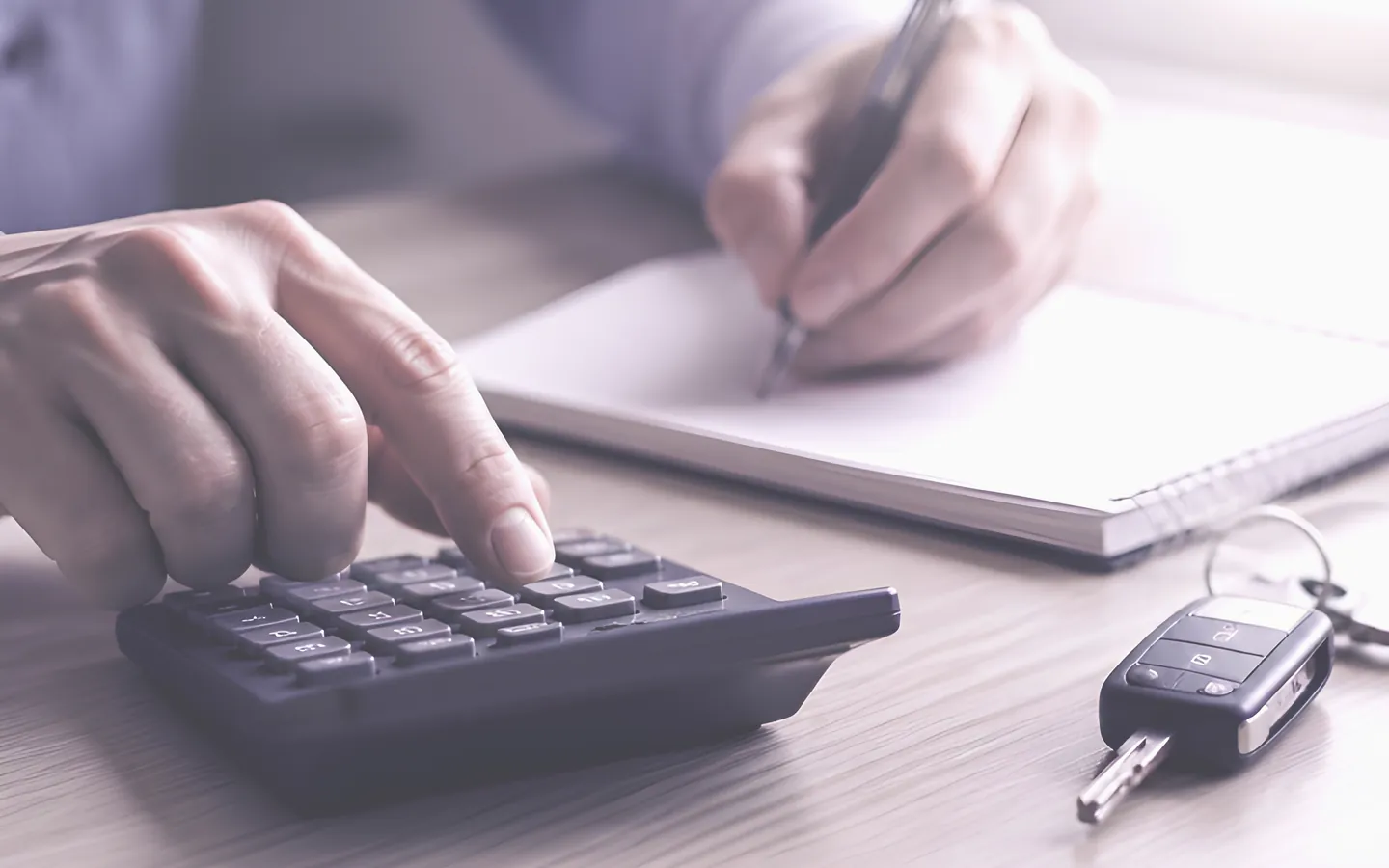 Hands using a calculator beside car keys