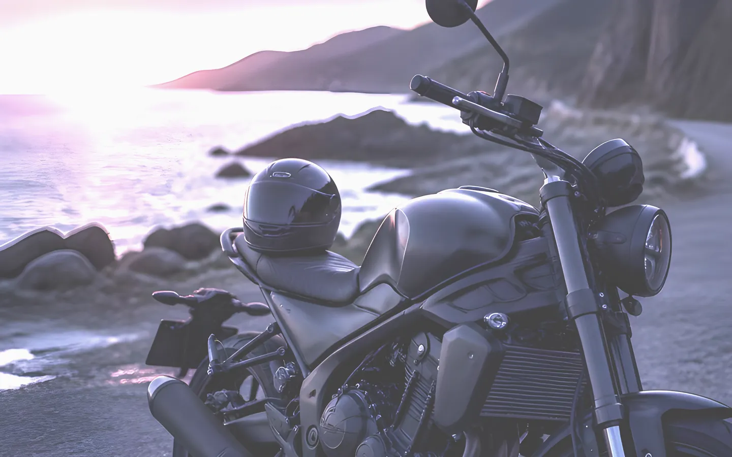 Motorbike and helmet on a coastal road at sunset
